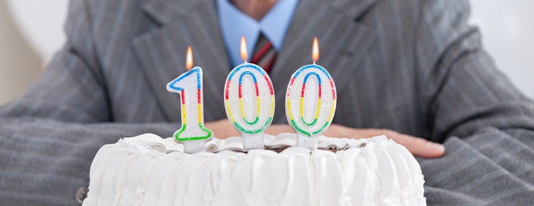 A man sitting behind a cake with “100” birthday candles.