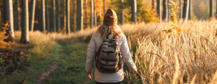 A woman with a backpack walking through woodland.
