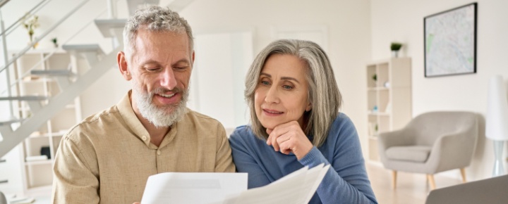 A senior couple sit at a laptop comparing multiple documents