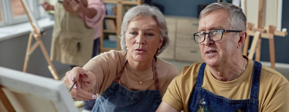 An older couple painting at an easel together.
